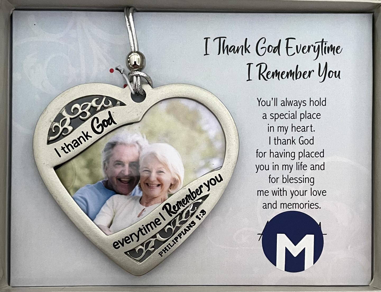 I THANK GOD PHOTO ORNAMENT. METAL HEART IN SILVER ENAMEL FINISH. PHOTO SIZE 3 X 2.75 IN. HANGS ON STRETCHY SILVER CORD WITH SILVER BEAD. OVERALL SIZE 3.5 X3 IN. WINDOW BOXED