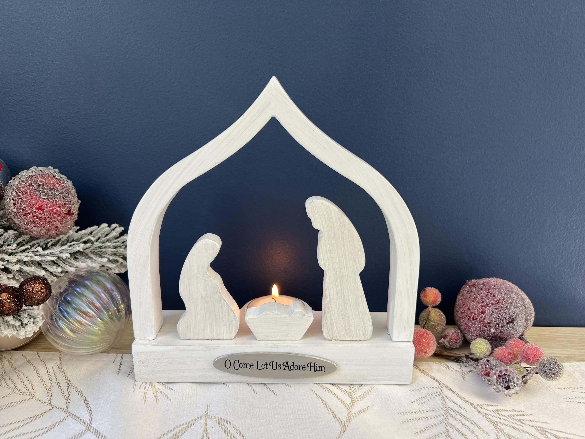 O COME LET US ADORE HIM CANDLE HOLDER. HANDCRAFTED WOOD CRECHE AND THREE PIECE NATIVITY IN WHITEWASH ADORNED WITH CAST METAL PLAQUE IN SILVER ENAMEL. COMPLETE WITH TEA LIGHT 7IN H X 6.5IN W 
